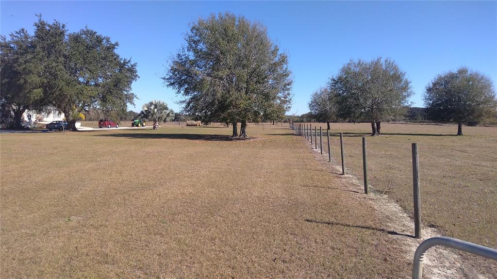 A large, grassy field features a wooden fence line and several mature trees under blue skies — 12051 AVON PARK CUT OFF ROAD, FORT MEADE, FL