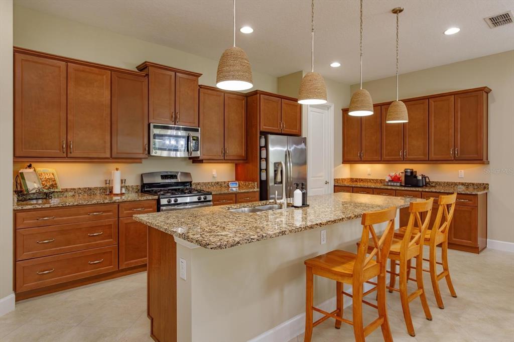 A kitchen features wood cabinets, granite countertops, a center island with stools, and pendant lighting — 1634 VICTORIA GARDENS DRIVE, DELAND, FL