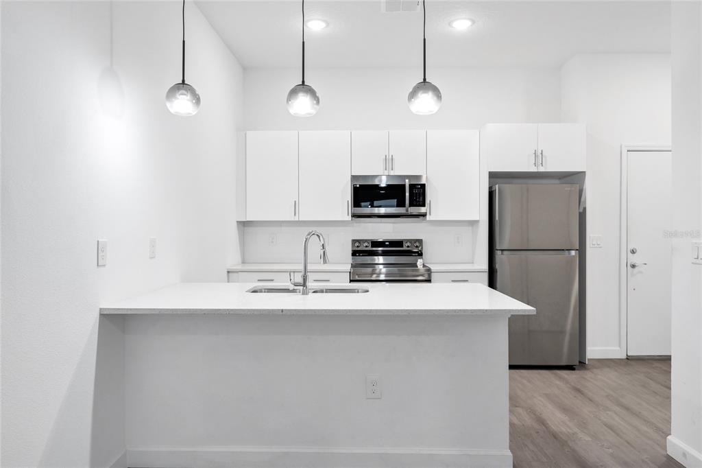 A modern kitchen features white cabinetry, stainless steel appliances, and a central island with seating — 485 FAMAGUSTA DRIVE, DAVENPORT, FL
