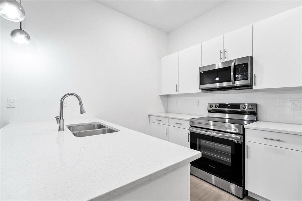 A modern kitchen features white cabinets, stainless steel appliances, and a white quartz island — 485 FAMAGUSTA DRIVE, DAVENPORT, FL