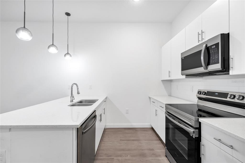 A modern kitchen features white cabinets, stainless steel appliances, and a white quartz island countertop — 485 FAMAGUSTA DRIVE, DAVENPORT, FL