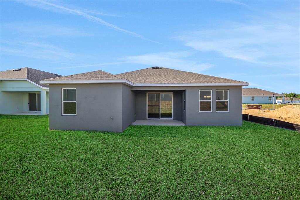 The rear exterior of a gray stucco house features a covered patio and sliding glass doors — 2866 SUPERMARINE ROAD, TAVARES, FL
