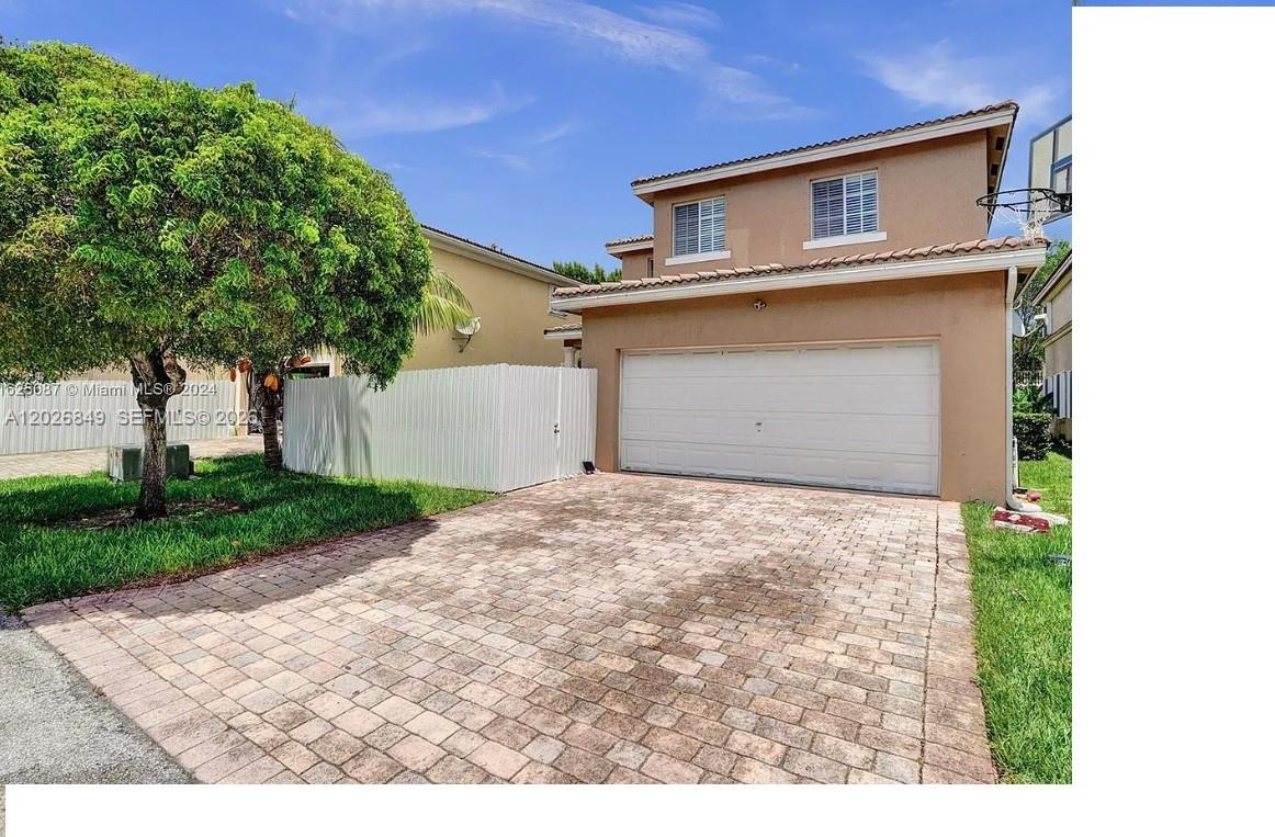 A two-story house features a tan stucco exterior, a white garage door, and a paved driveway — HOMESTEAD, FL