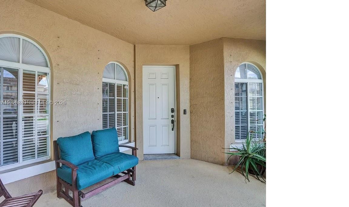 A covered entryway features a white door, arched windows, and a teal loveseat — HOMESTEAD, FL