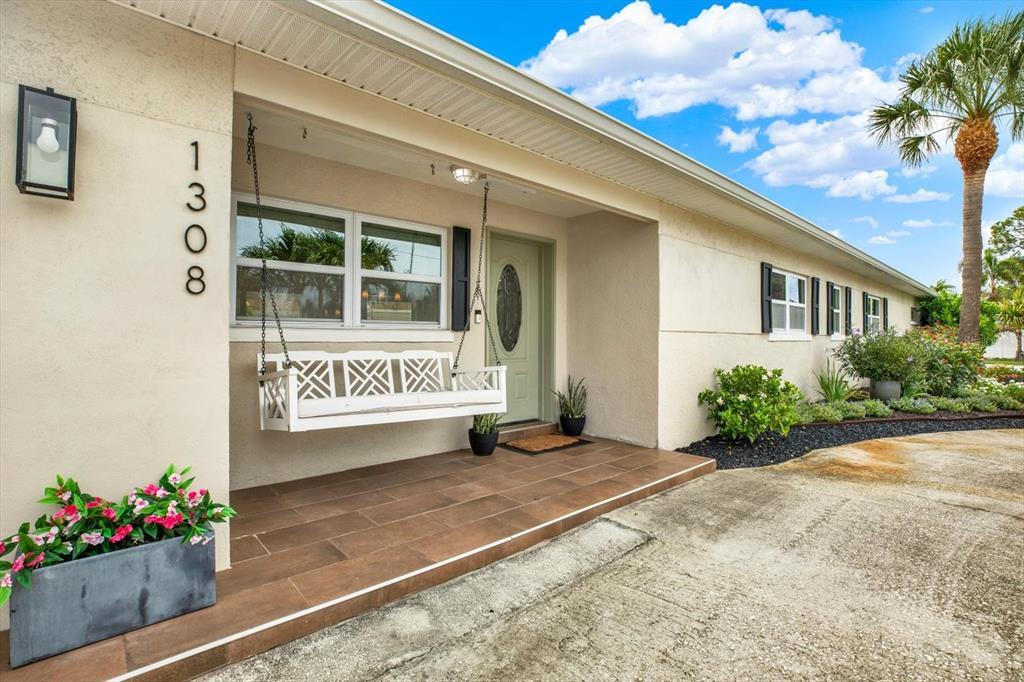 A beige house exterior features a front porch with a white hanging swing — 1308 MARION DRIVE S, ST PETERSBURG, FL