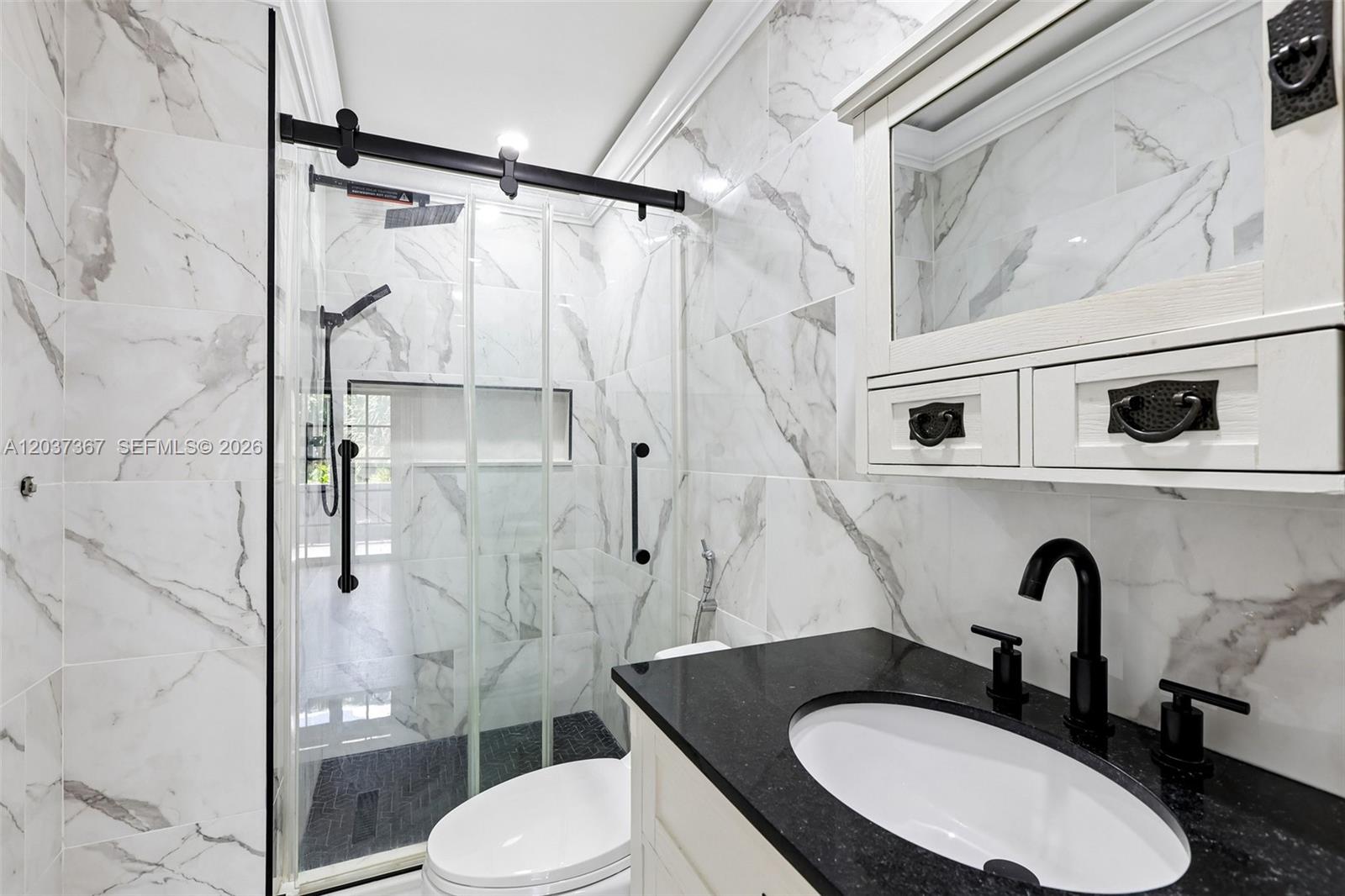 A bathroom features a glass-enclosed shower, marble-patterned wall tiles, and a black granite vanity countertop — 86 Ann Lee Ln, Tamarac FL 33319, TAMARAC, FL