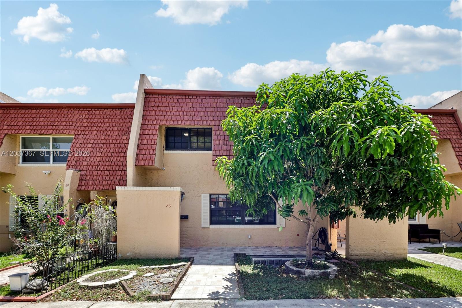 A two-story townhouse features a red shingled mansard roof, tan stucco walls, and a tree — 86 Ann Lee Ln, Tamarac FL 33319, TAMARAC, FL