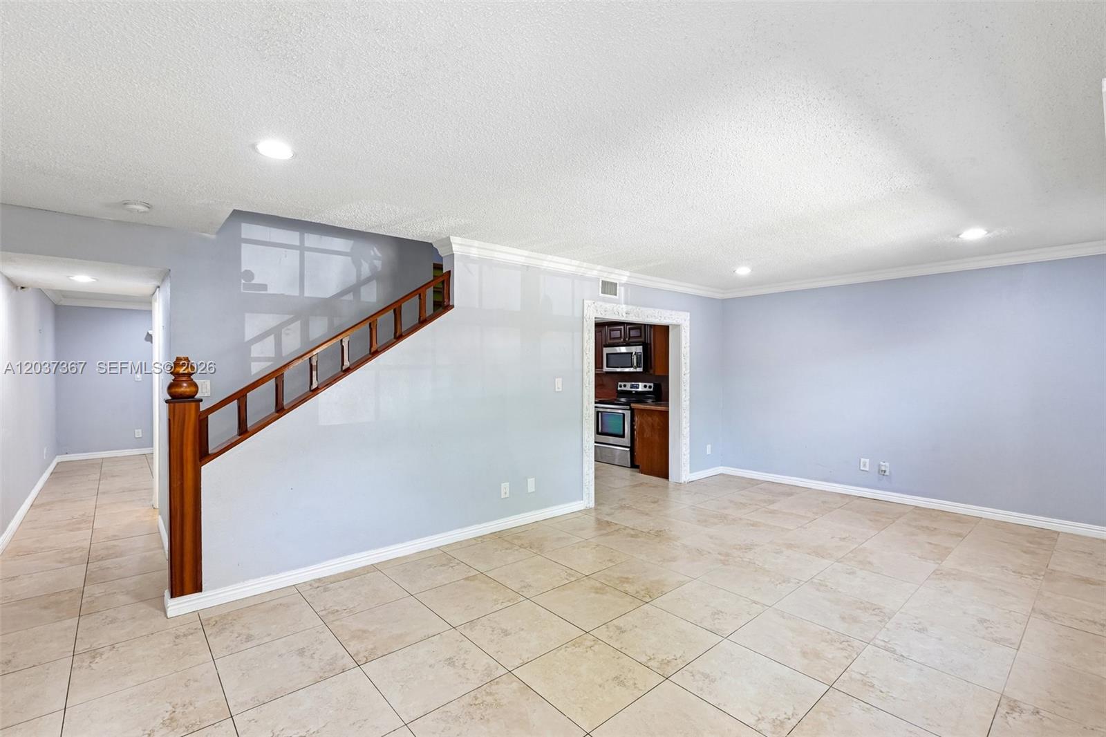 An open living area features light-colored tile flooring, a wooden staircase, and a kitchen doorway — 86 Ann Lee Ln, Tamarac FL 33319, TAMARAC, FL