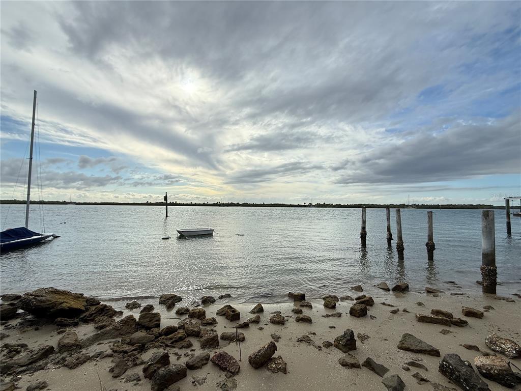 A small boat floats in a bay near a rocky shoreline with wooden pilings — 1602 N INDIAN RIVER ROAD, NEW SMYRNA BEACH, FL