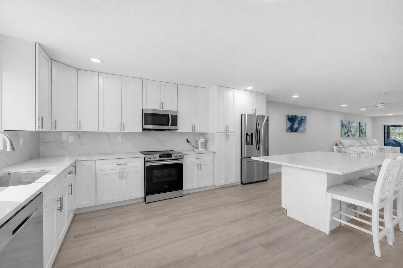 A modern kitchen features white cabinets, stainless steel appliances, and a large marble-topped island — 300 N Highway A1a # 105d, Jupiter FL 33477, JUPITER, FL
