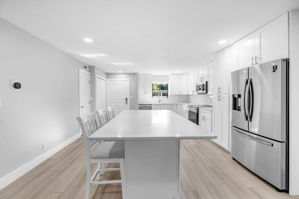 A modern kitchen features white cabinetry, a large marble-topped island, and stainless steel appliances — 300 N Highway A1a # 105d, Jupiter FL 33477, JUPITER, FL