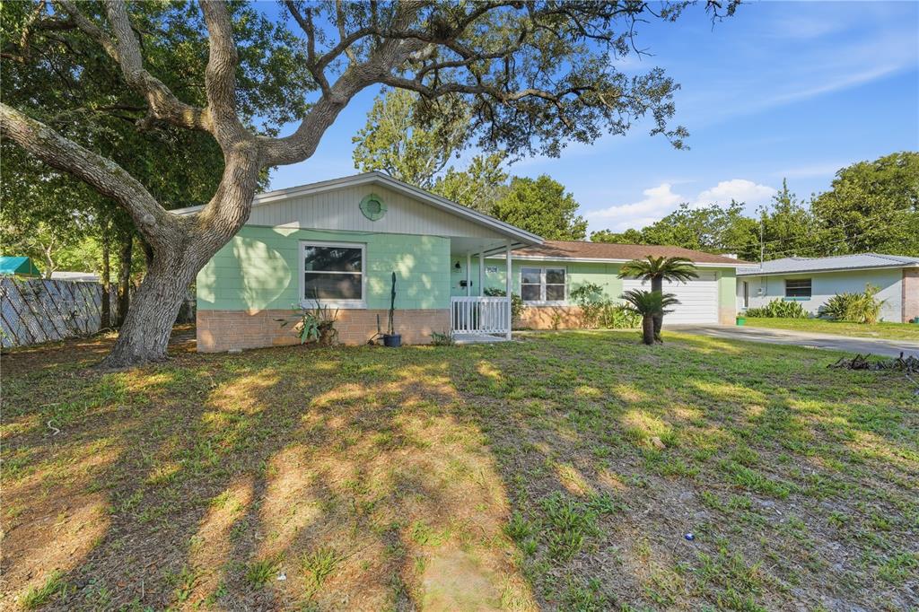 A single-story house with light green siding and a brick base sits under a large tree — 1528 VALENCIA AVENUE, DAYTONA BEACH, FL