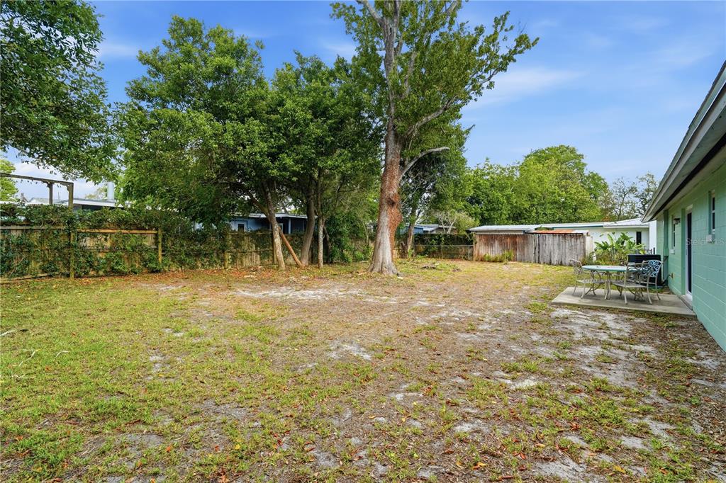 A backyard with a concrete patio, a large tree, and a wooden fence — 1528 VALENCIA AVENUE, DAYTONA BEACH, FL