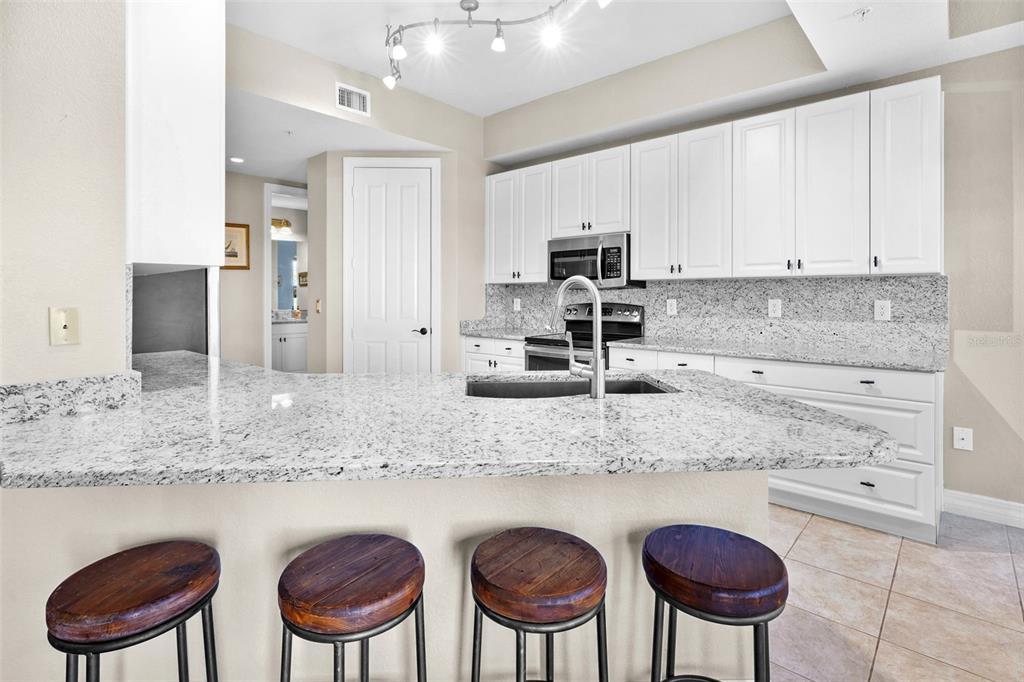 A kitchen features white cabinets, granite countertops, a breakfast bar, and four wooden bar stools — 98 VIVANTE BOULEVARD UNIT 410, PUNTA GORDA, FL