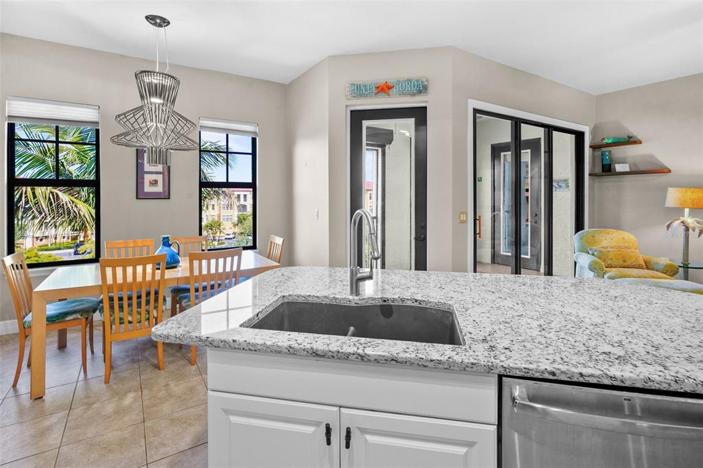 A kitchen island with a granite countertop overlooks a dining area and a living space — 98 VIVANTE BOULEVARD UNIT 410, PUNTA GORDA, FL