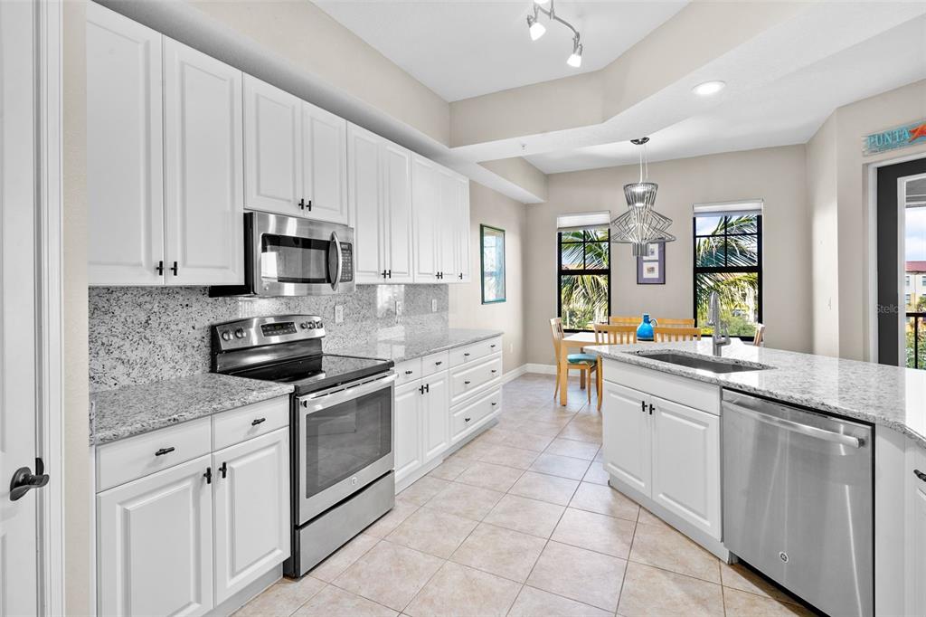 A kitchen with white cabinets, granite countertops, stainless steel appliances, and an adjacent dining area — 98 VIVANTE BOULEVARD UNIT 410, PUNTA GORDA, FL