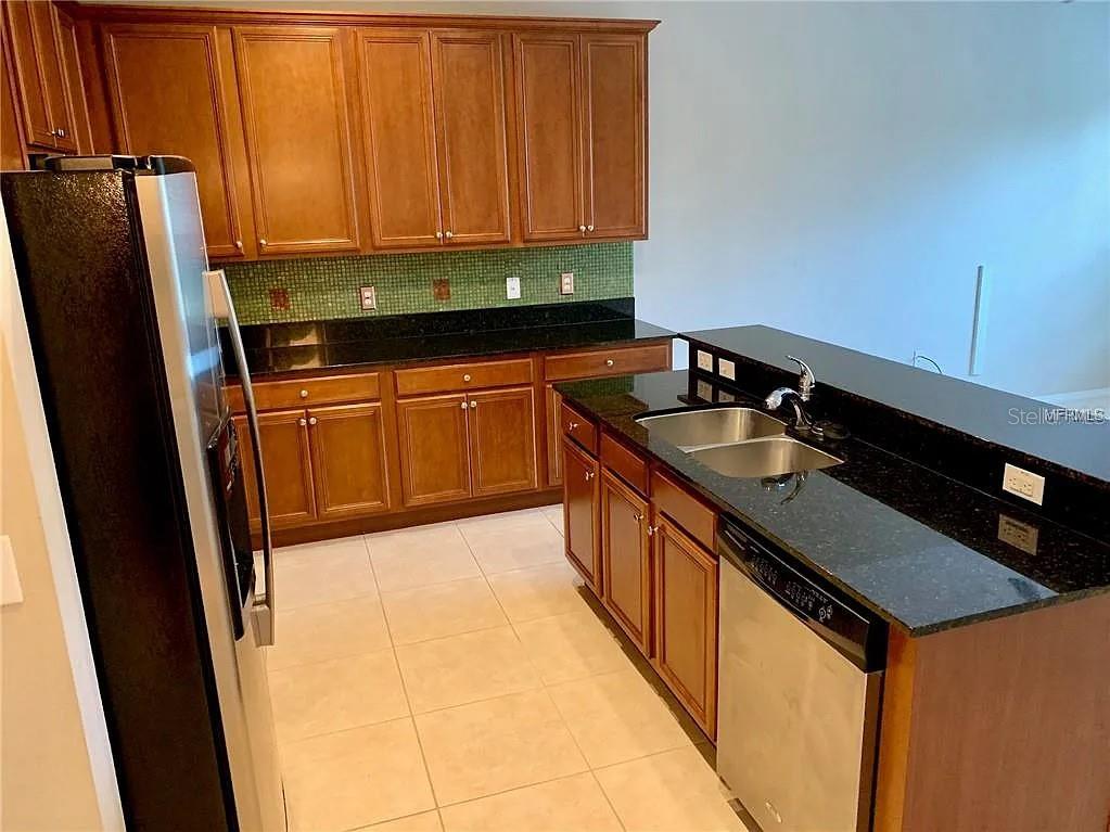 A kitchen features wood cabinets, black countertops, a stainless steel refrigerator, and a dishwasher — 1781 GRAND RUE DRIVE, CASSELBERRY, FL
