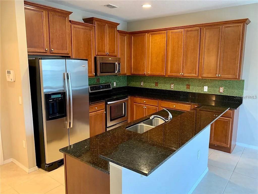 A kitchen features wood cabinets, dark granite countertops, stainless steel appliances, and a green backsplash — 1781 GRAND RUE DRIVE, CASSELBERRY, FL