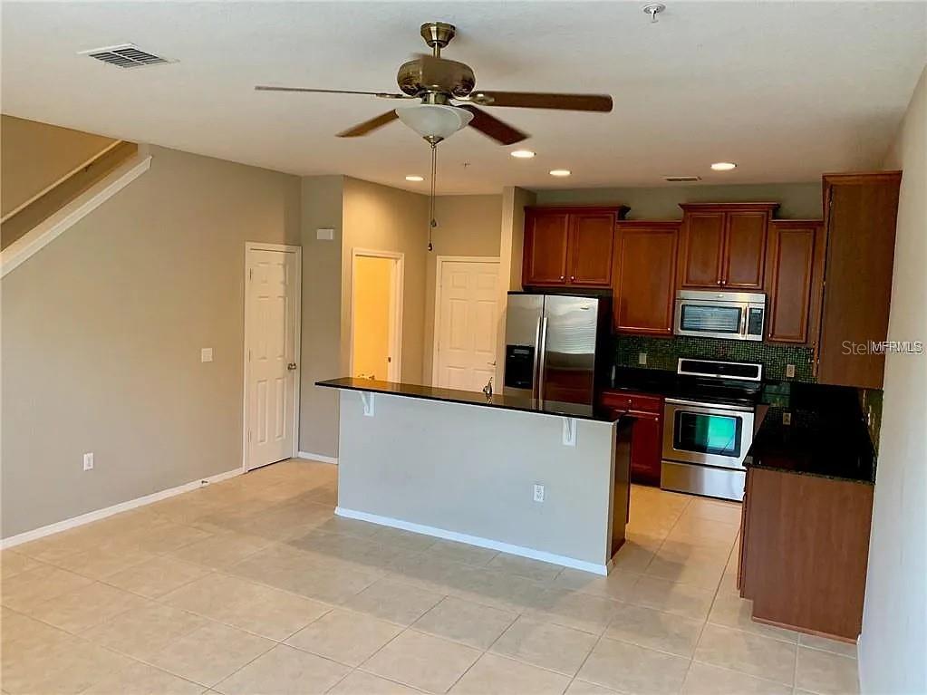 A kitchen with dark wood cabinets and stainless steel appliances overlooks a tiled living area — 1781 GRAND RUE DRIVE, CASSELBERRY, FL