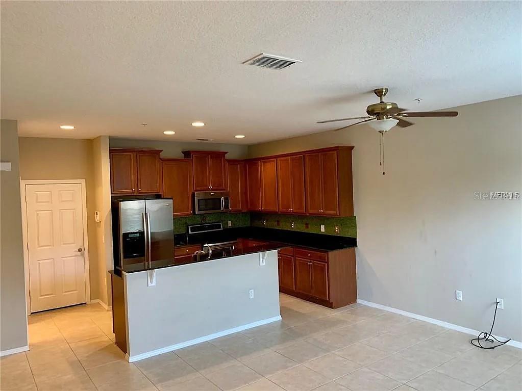 A kitchen features dark wood cabinets, black countertops, stainless steel appliances, and tile flooring — 1781 GRAND RUE DRIVE, CASSELBERRY, FL