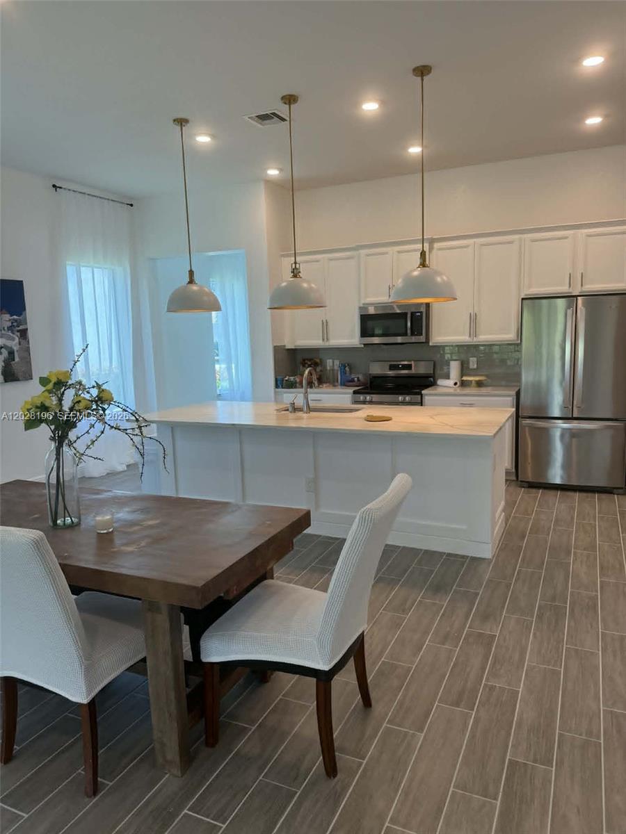 A kitchen features white cabinets, a marble-topped island, three pendant lights, and wood-look tile floors — 4710 SW Ardsley Dr, Stuart FL 34997, STUART, FL