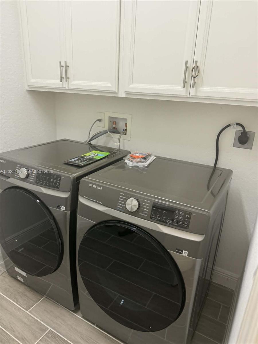 A laundry room features two gray Samsung appliances beneath white cabinets and gray tile flooring — 4710 SW Ardsley Dr, Stuart FL 34997, STUART, FL