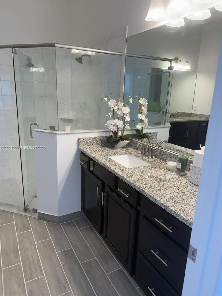 A bathroom features a dark wood vanity with granite countertops, a glass shower, and tile flooring — 4710 SW Ardsley Dr, Stuart FL 34997, STUART, FL