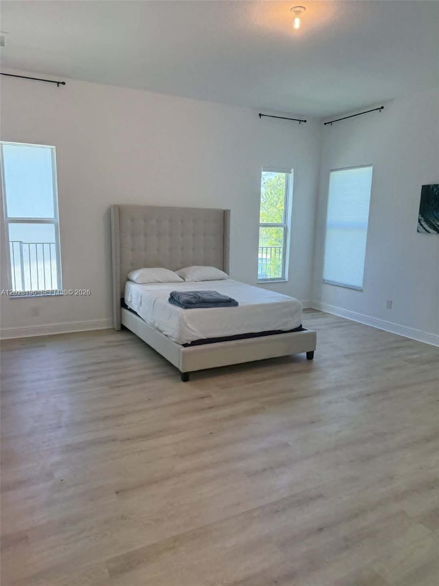 A bedroom features light wood-look flooring, white walls, and a beige upholstered bed frame — 4710 SW Ardsley Dr, Stuart FL 34997, STUART, FL