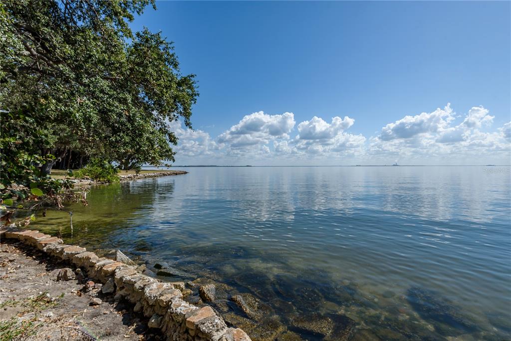 A stone retaining wall borders a calm body of water beneath a clear blue sky — 6210 BAYSHORE BOULEVARD, TAMPA, FL