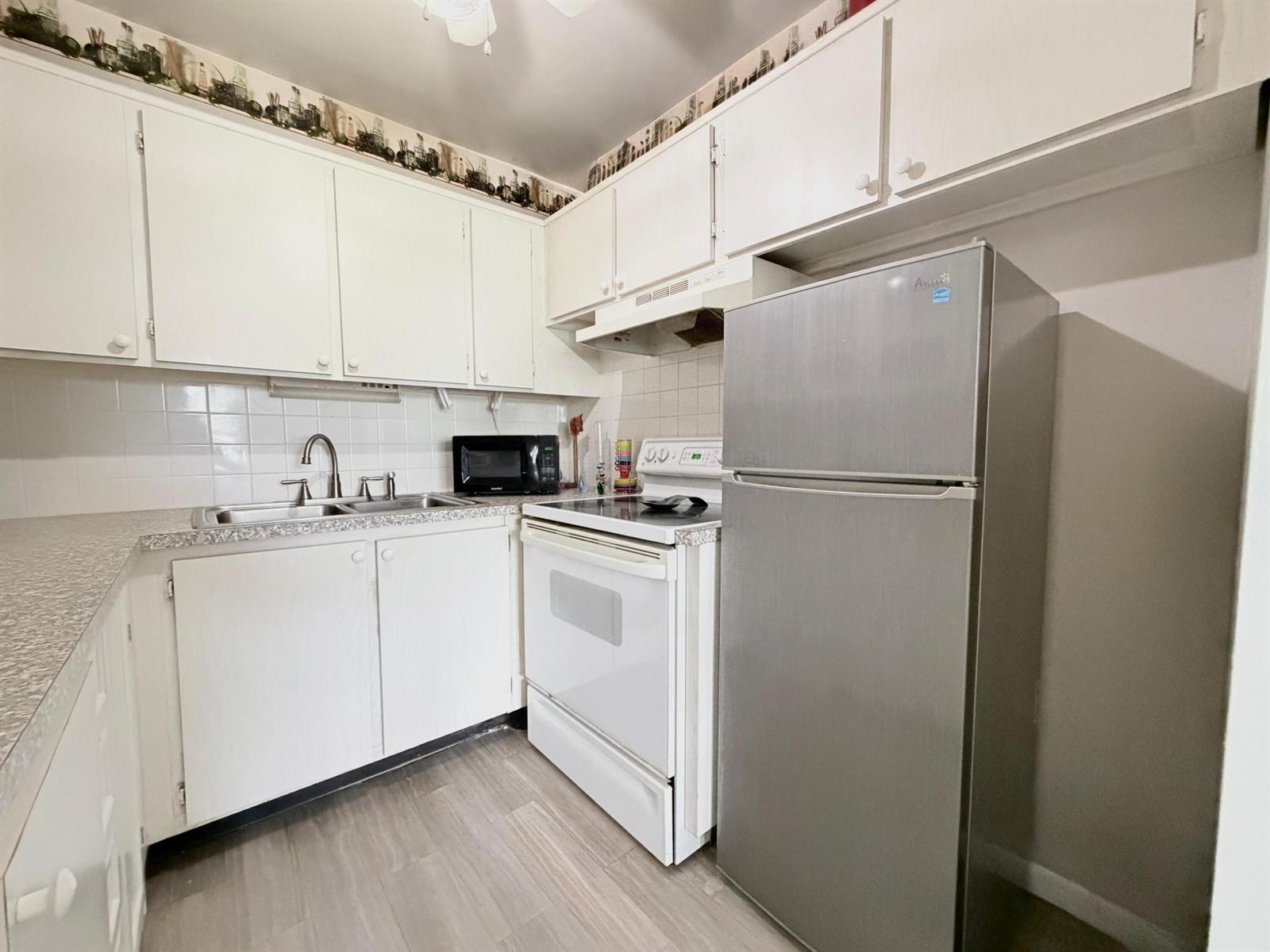 A small kitchen features white cabinets, a stainless steel refrigerator, and a white electric stove — 62 Easthampton C, West Palm Beach FL 33417, WEST PALM BEACH, FL