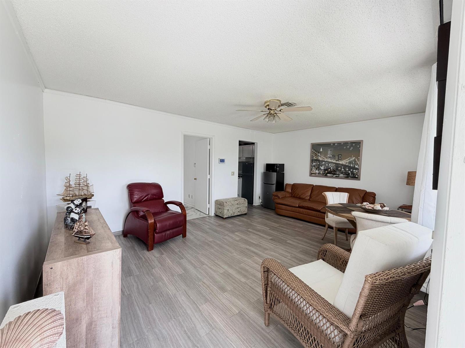 A living room features wood-look flooring, a ceiling fan, and a mix of seating furniture — 62 Easthampton C, West Palm Beach FL 33417, WEST PALM BEACH, FL