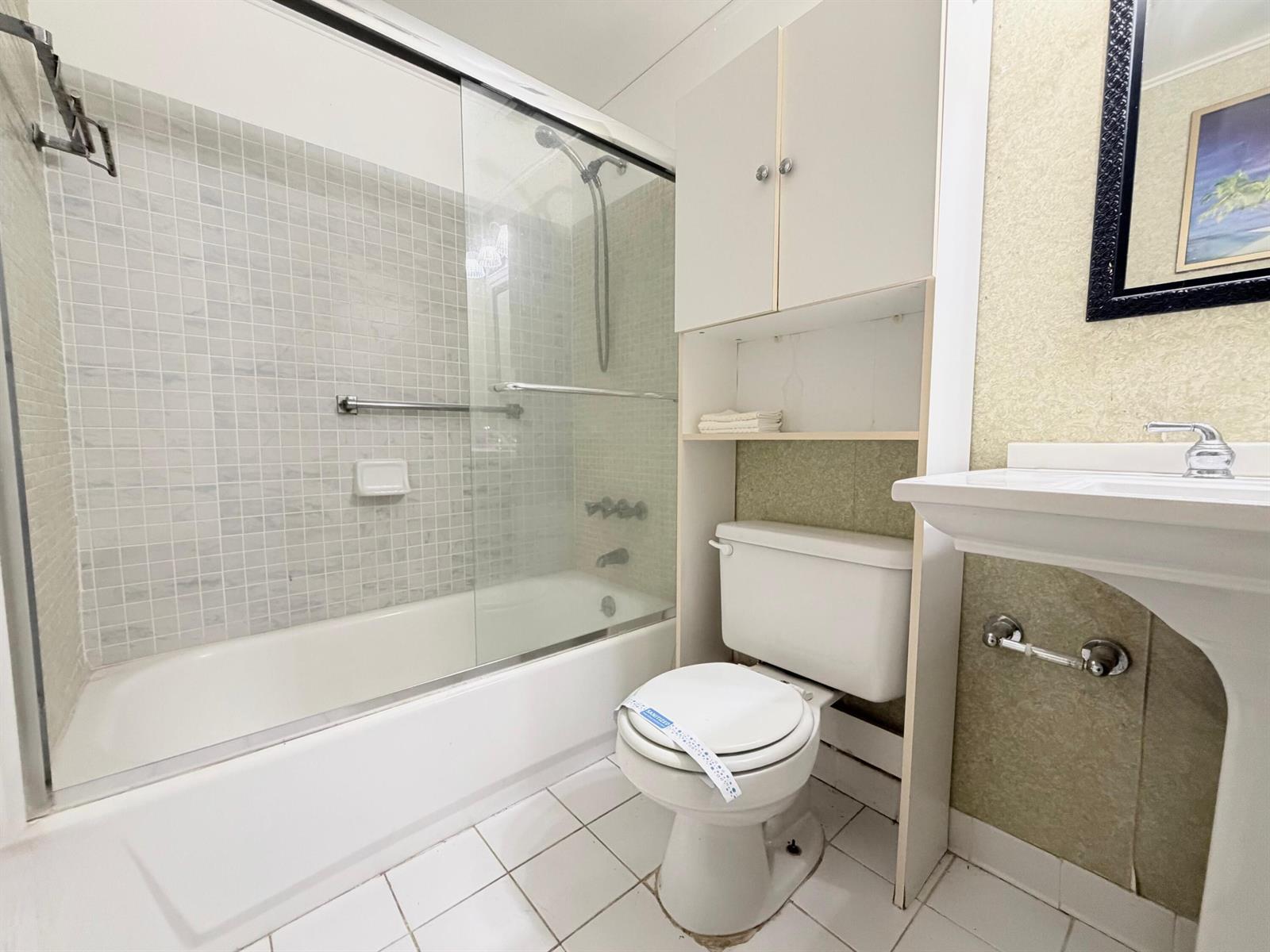 A bathroom features a white toilet, a pedestal sink, and a tiled shower-tub combination — 62 Easthampton C, West Palm Beach FL 33417, WEST PALM BEACH, FL