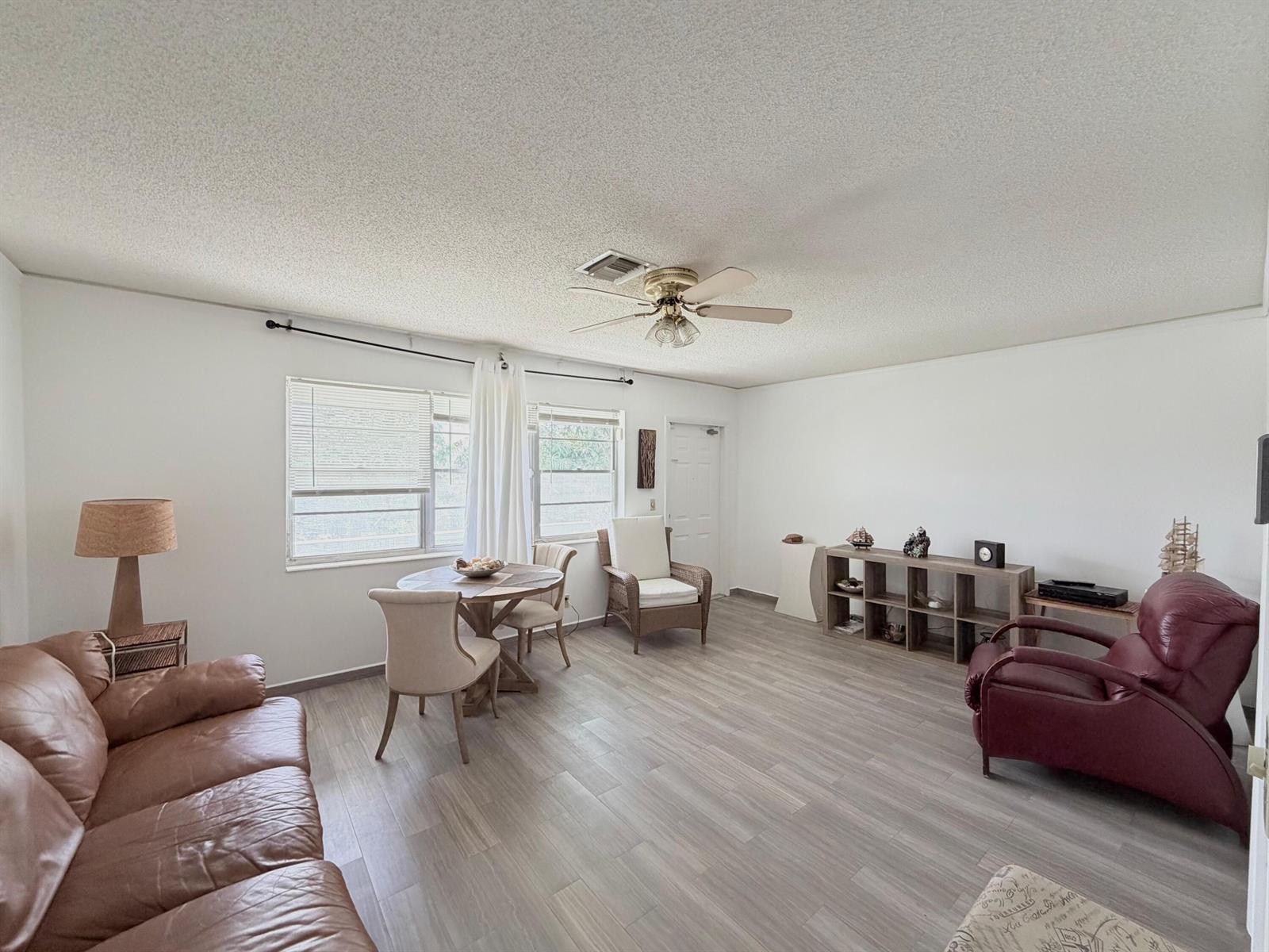 A living room with light wood-look flooring, a ceiling fan, and a small dining area — 62 Easthampton C, West Palm Beach FL 33417, WEST PALM BEACH, FL