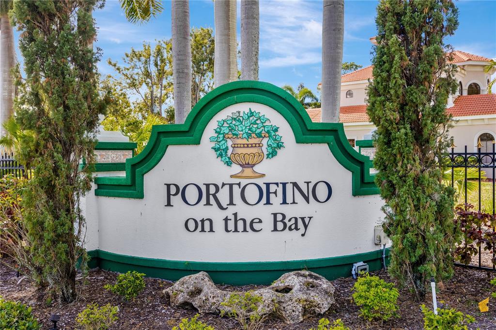 A white community entrance sign with green trim reads Portofino on the Bay — 1680 ASSISI DRIVE UNIT 13, SARASOTA, FL