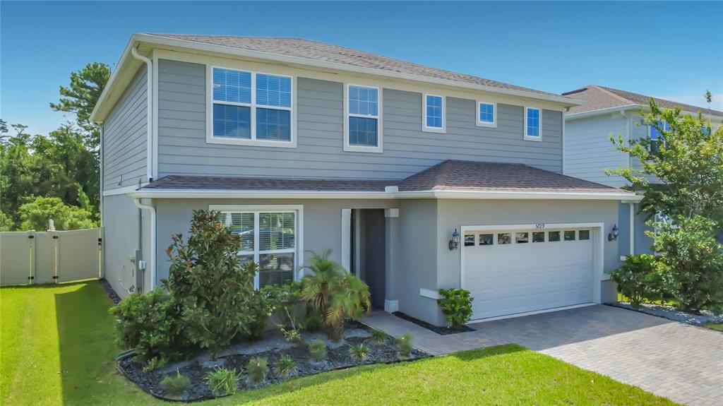 A two-story house with gray siding, a white garage door, and a landscaped front yard — 5729 WOODEN PINE DRIVE, ORLANDO, FL
