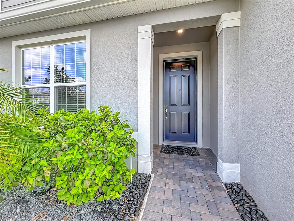 A gray house exterior features a dark blue front door and a paved walkway — 5729 WOODEN PINE DRIVE, ORLANDO, FL