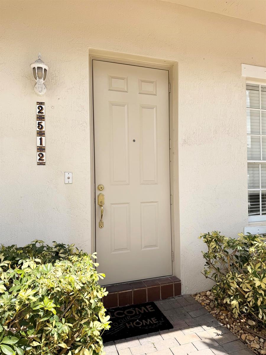 A beige front door with a vertical address plaque is flanked by bushes and a window — 2512 NW 4th Street, Boynton Beach FL 33426, BOYNTON BEACH, FL