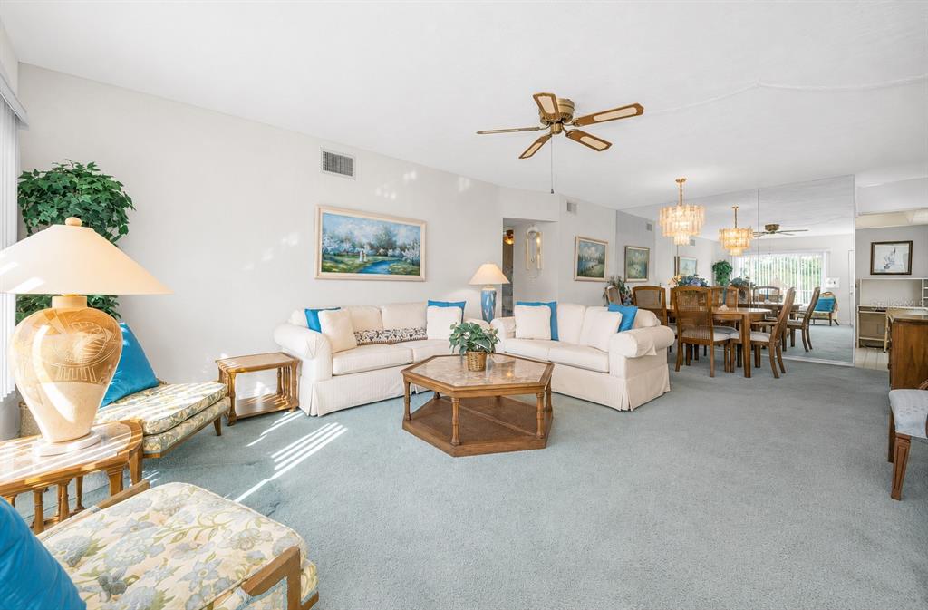 A living room with light blue carpeting, two white sofas, and a dining area beyond — 2001 WORLD PARKWAY BOULEVARD UNIT 39, CLEARWATER, FL