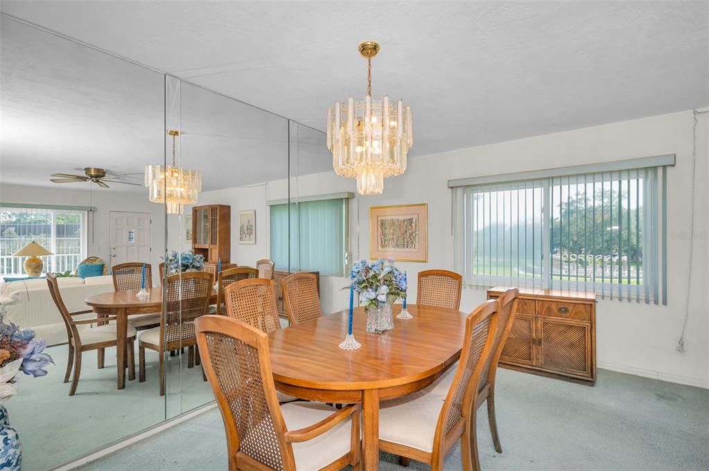 A dining room features a wooden table, cane-back chairs, a crystal chandelier, and mirrored walls — 2001 WORLD PARKWAY BOULEVARD UNIT 39, CLEARWATER, FL