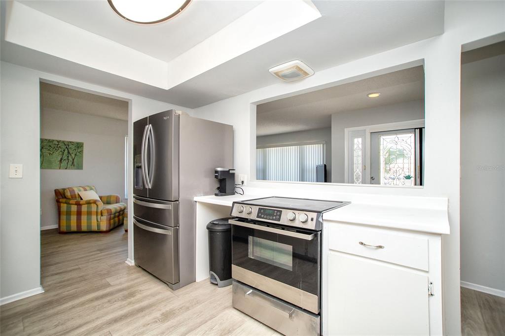 A kitchen features stainless steel appliances, white cabinetry, and a pass-through window to another room — 1647 BENTLEY COURT, PALM HARBOR, FL