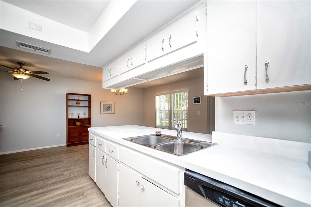 A kitchen with white cabinets, a double-basin sink, and a view into the dining area — 1647 BENTLEY COURT, PALM HARBOR, FL