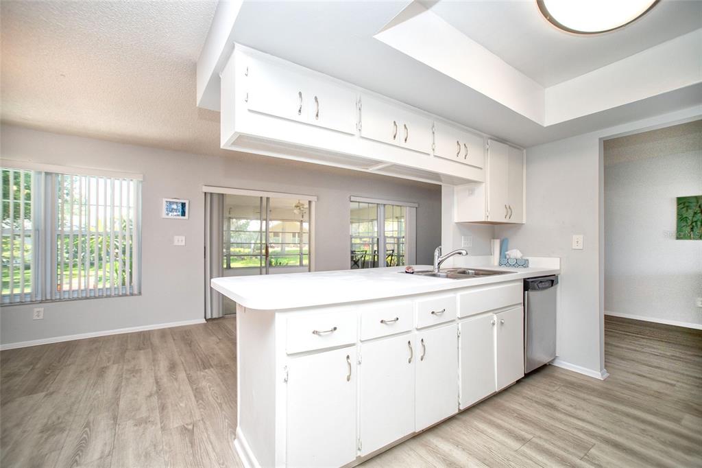 A kitchen with white cabinets, a peninsula sink, and light wood-look flooring — 1647 BENTLEY COURT, PALM HARBOR, FL