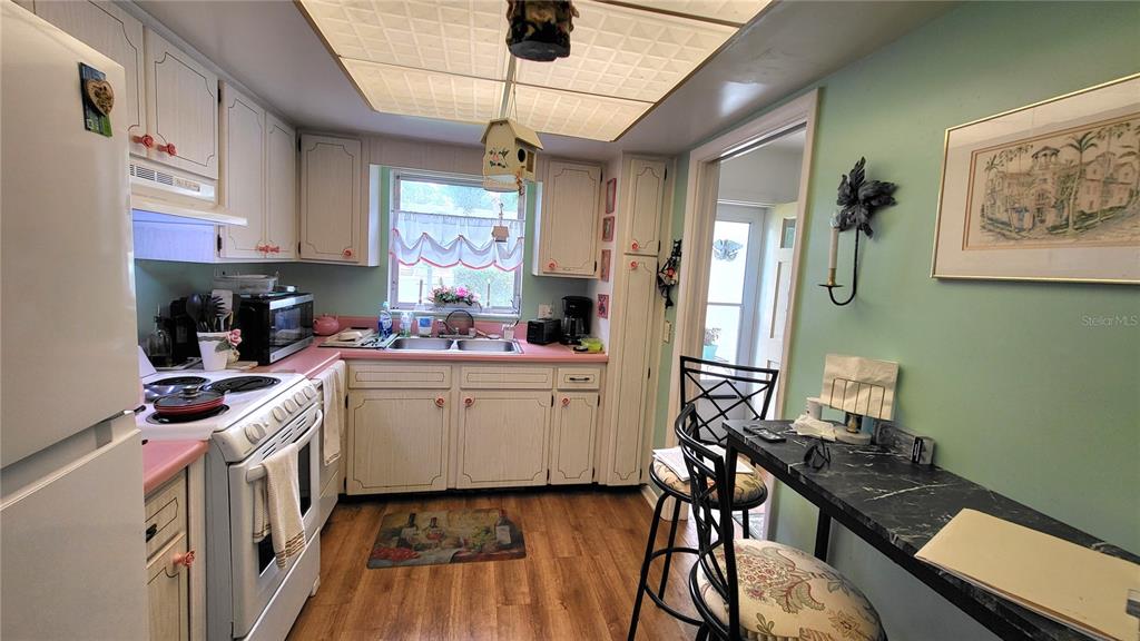 A kitchen features white cabinets, pink countertops, a drop ceiling, and a small breakfast bar — 1421 NORMANDY PARK DRIVE UNIT 4, CLEARWATER, FL