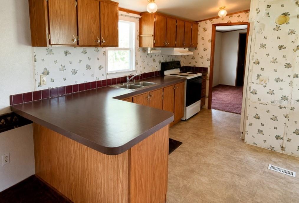 A kitchen with wood cabinets, dark laminate countertops, floral wallpaper, and a white stove — 1142 SW JIM CLARK ROAD, MADISON, FL