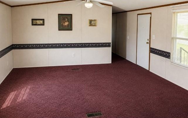 An empty living room features maroon carpeting, beige paneled walls with a border, and a ceiling fan — 1142 SW JIM CLARK ROAD, MADISON, FL