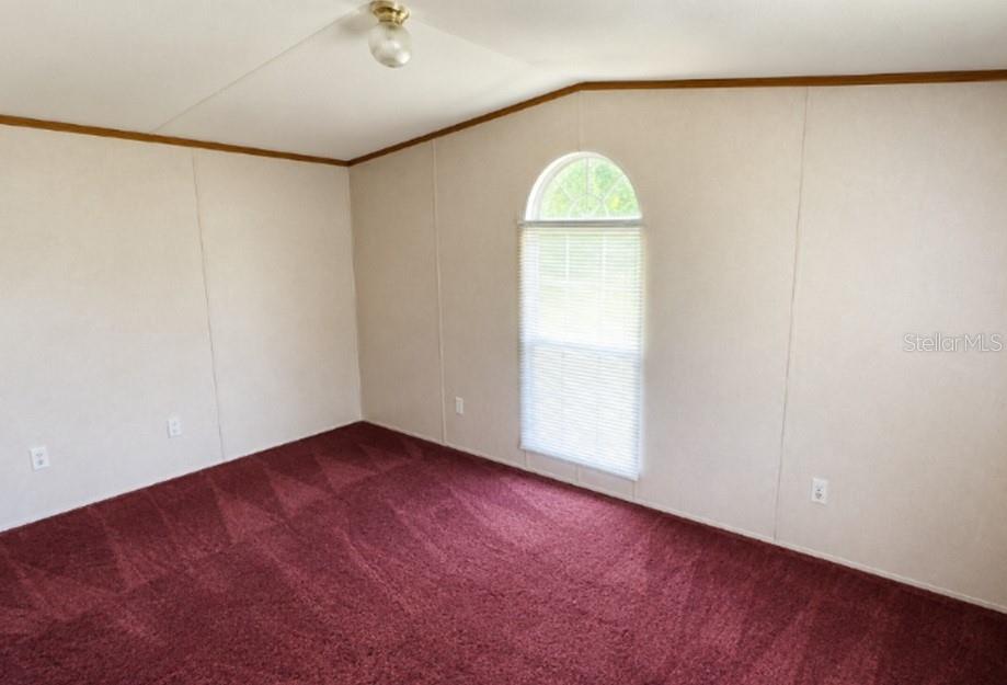 An empty room features beige walls, red carpeting, and an arched window with blinds — 1142 SW JIM CLARK ROAD, MADISON, FL