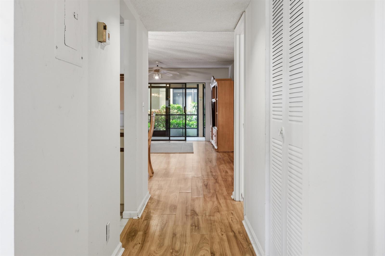A hallway with wood-look flooring leads to a living area with a sliding glass door — 10118 Mangrove Drive # 105, Boynton Beach FL 33437, BOYNTON BEACH, FL
