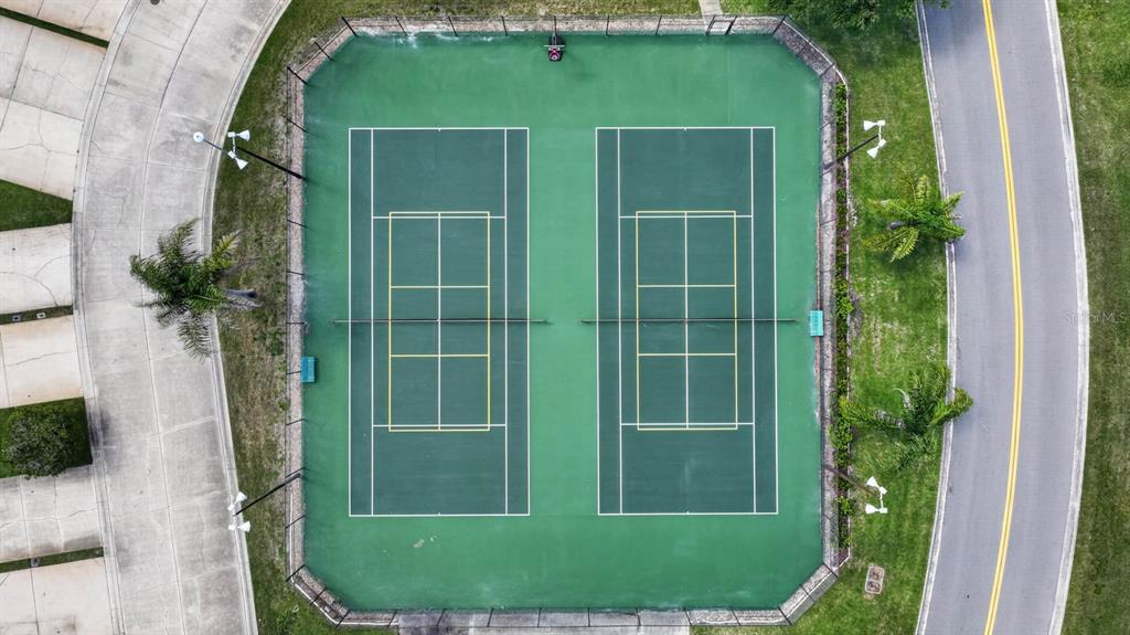 An aerial view shows two tennis courts enclosed by a fence next to a road — 357 CASTLEWOOD LANE, NEW SMYRNA BEACH, FL