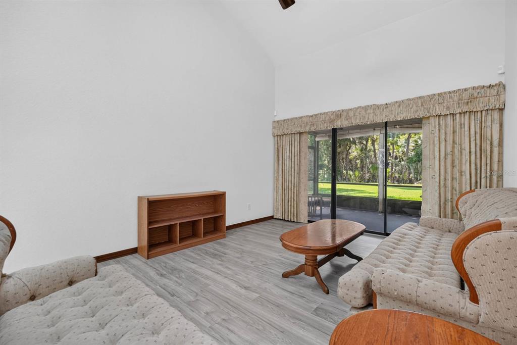 A living room features light wood-look flooring, a wooden bookshelf, and sliding glass doors — 357 CASTLEWOOD LANE, NEW SMYRNA BEACH, FL