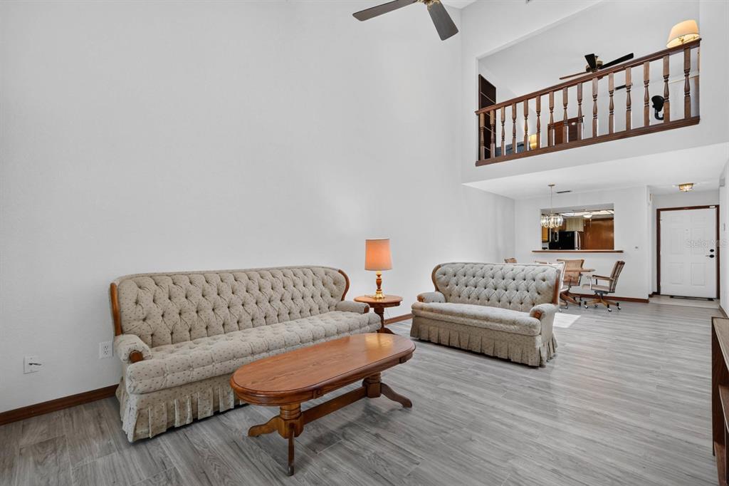 A living room with high ceilings, tufted sofas, a wooden coffee table, and wood-look flooring — 357 CASTLEWOOD LANE, NEW SMYRNA BEACH, FL